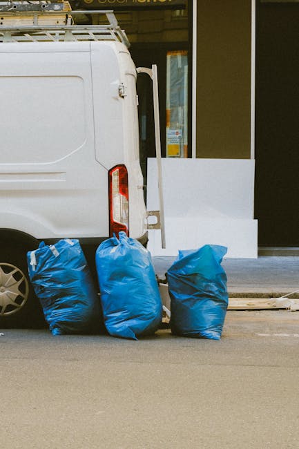In the foreground, three large blue plastic rubbish bags are placed on a paved surface, positioned close to the rear of a white utility van. The bags appear to be filled with waste material, with some
